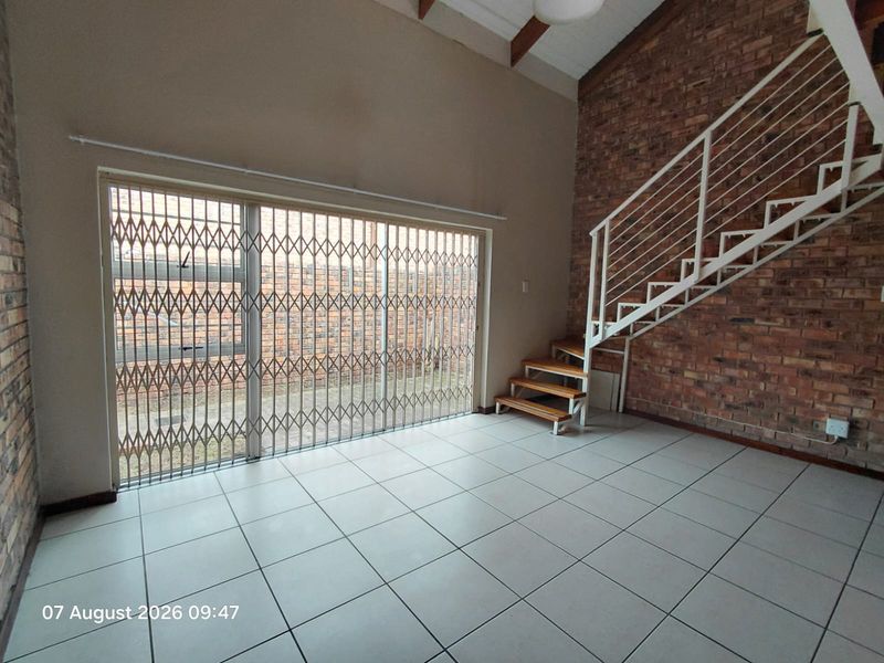 Spacious living area featuring exposed brick walls, tiled flooring, and a modern metal staircase leading to the upper level.