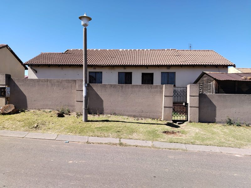 Front view of a single-story house featuring a tiled roof, perimeter wall with a metal gate, and a street-facing facade.