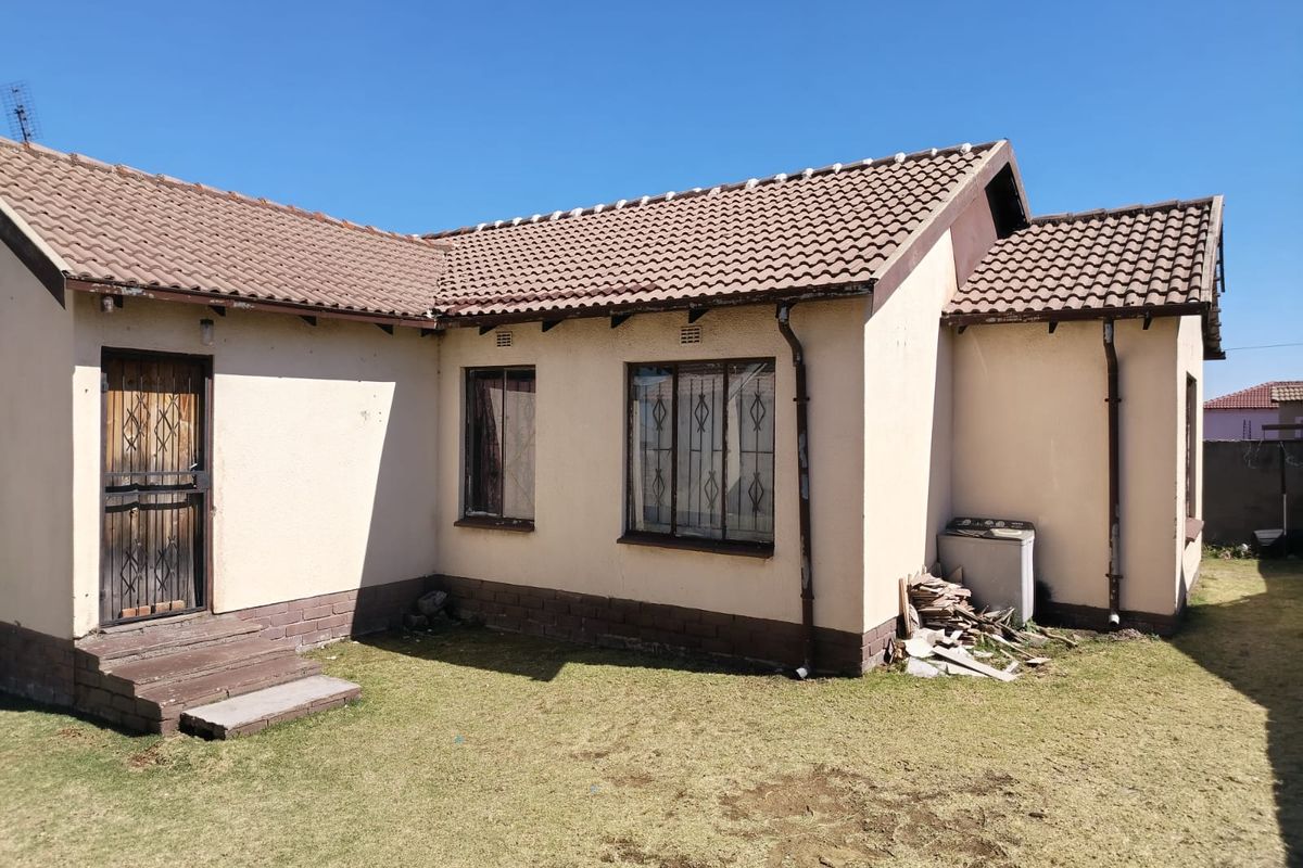 Rear view of a single-story house featuring a tiled roof, security gates, and burglar bars, set against a small lawn area.