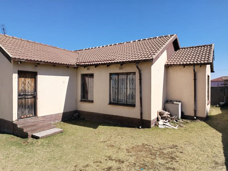 Rear view of a single-story house featuring a tiled roof, security gates, and burglar bars, set against a small lawn area.