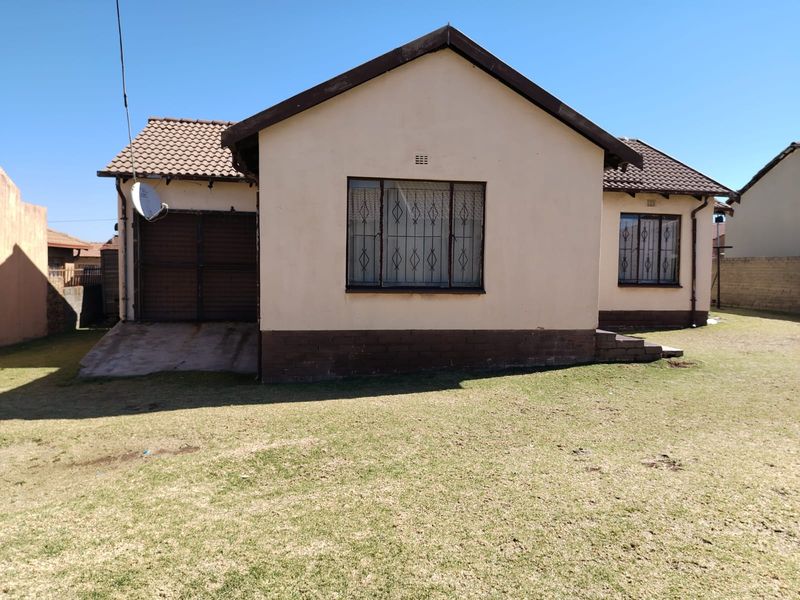 Rear view of a detached house featuring a tiled roof, security bars on windows, and an attached garage with a concrete driveway.