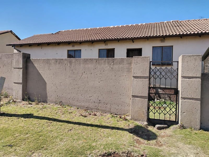 Rear view of the property featuring a concrete boundary wall with a metal security gate and a tiled roof structure.