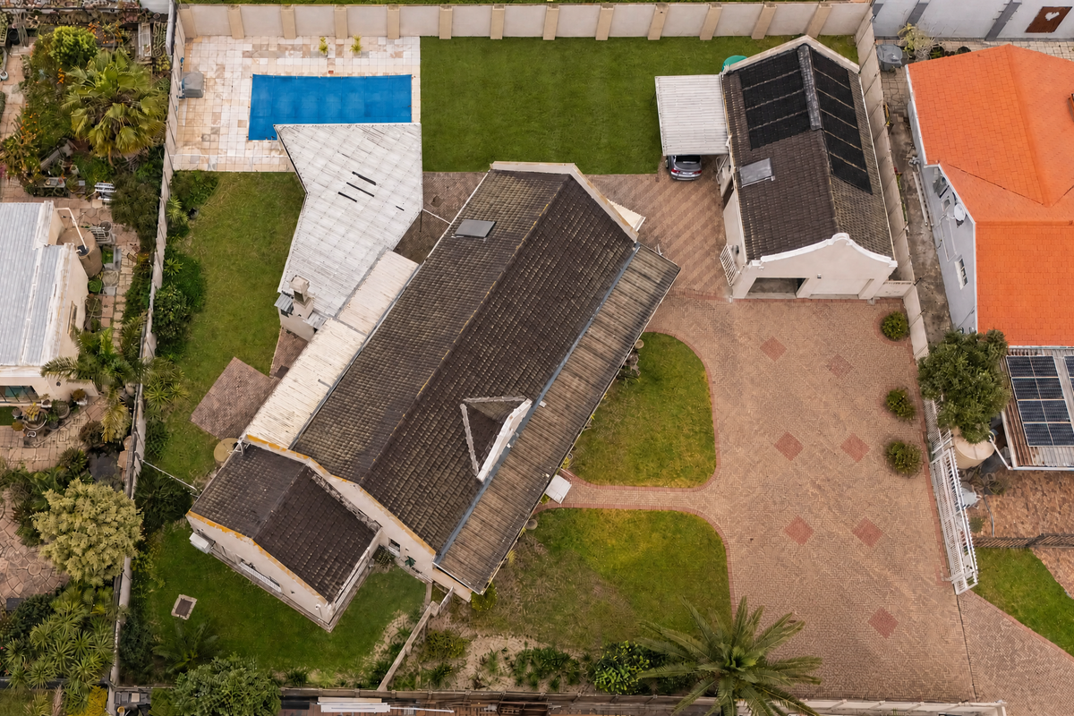 Aerial view of a residential property featuring a paved driveway, swimming pool, landscaped garden, and a main house with a tiled roof and solar panels.