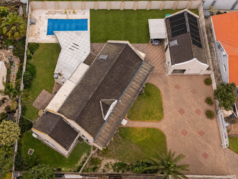 Aerial view of a residential property featuring a paved driveway, swimming pool, landscaped garden, and a main house with a tiled roof and solar panels.