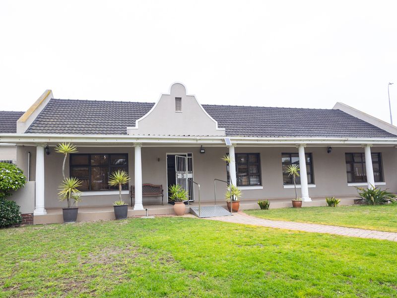 Front elevation of a single-story house featuring a covered veranda with classical columns, a paved walkway, and a gabled roof design.