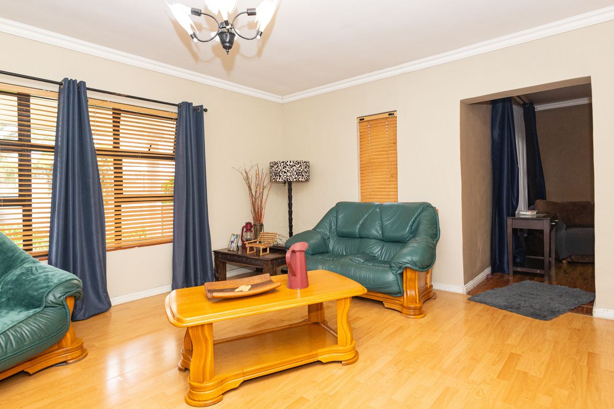 A living room featuring laminate flooring, crown molding, and large windows with venetian blinds, offering a functional and well-lit space.