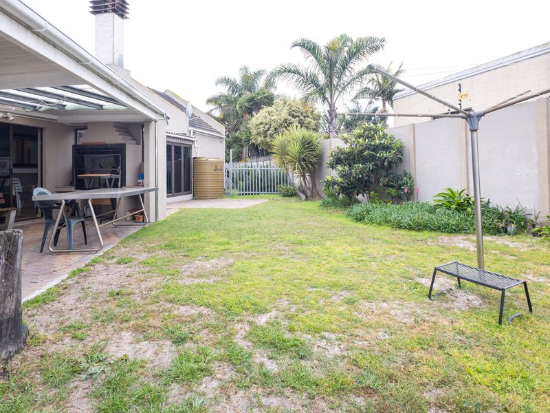 Rear garden featuring a covered patio with a built-in braai, paved entertainment area, water tank, and perimeter walling.