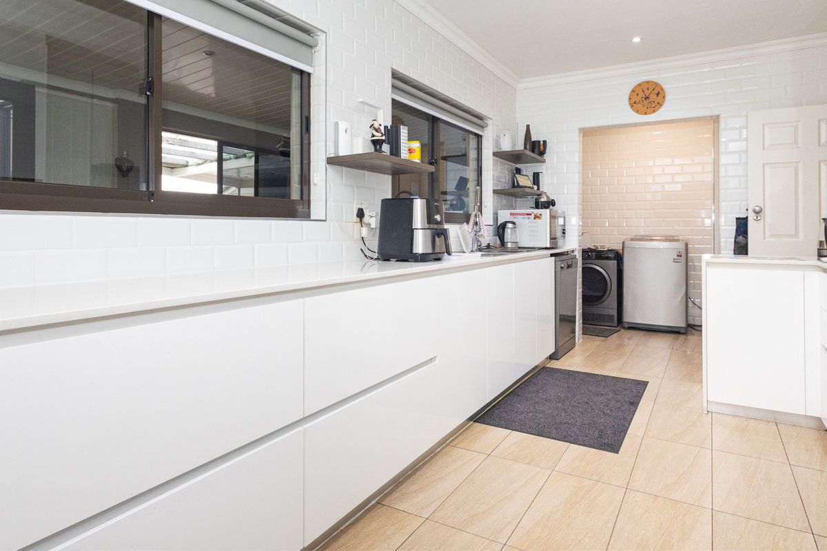 Modern kitchen featuring white handleless cabinetry, stone countertops, subway tile backsplash, and tiled flooring, with an adjacent utility area.