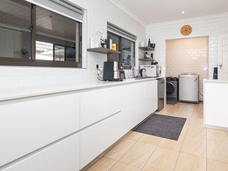 Modern kitchen featuring white handleless cabinetry, stone countertops, subway tile backsplash, and tiled flooring, with an adjacent utility area.