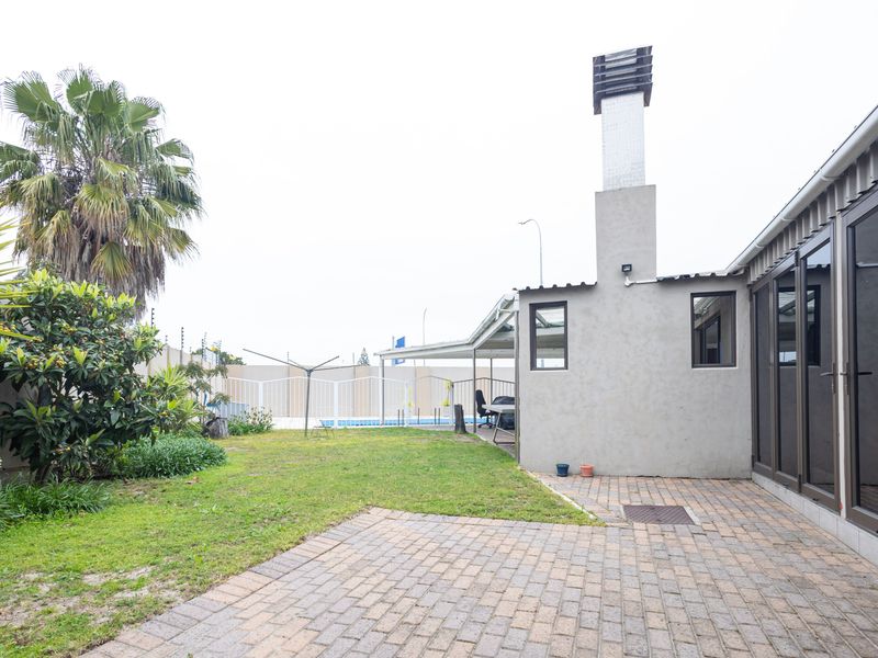 Rear garden area featuring a paved patio, external chimney, and sliding glass doors leading into the home, with a lawn and perimeter electric fencing.
