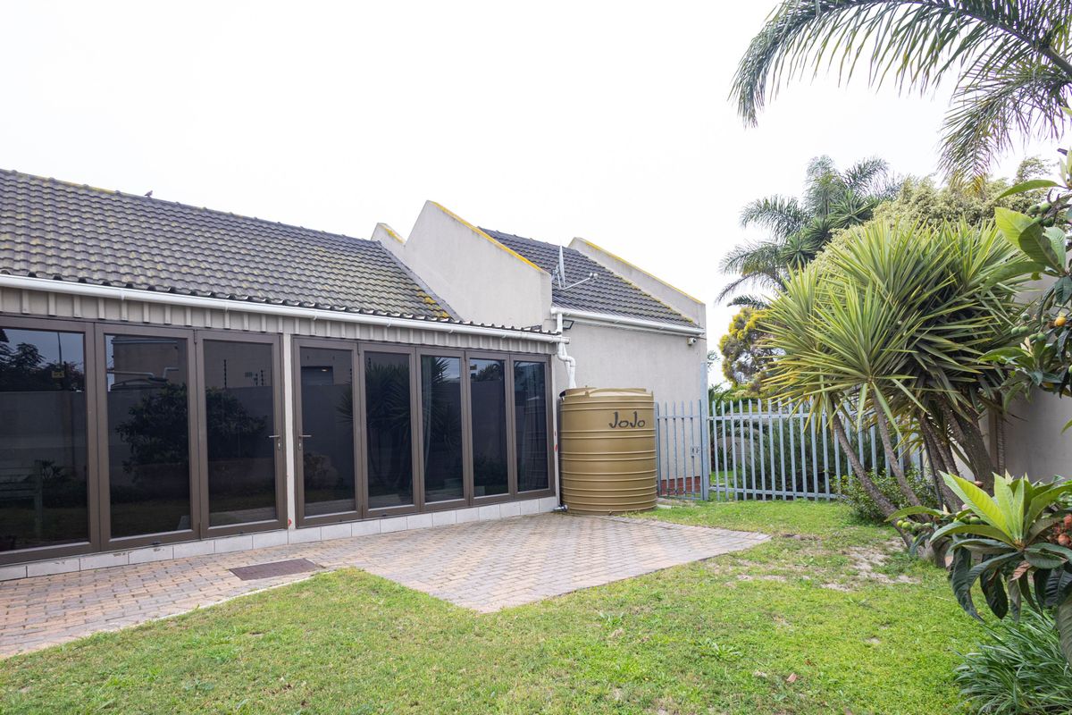 Rear view of the property featuring a paved patio area, large folding glass doors, and a water storage tank set within a private garden.