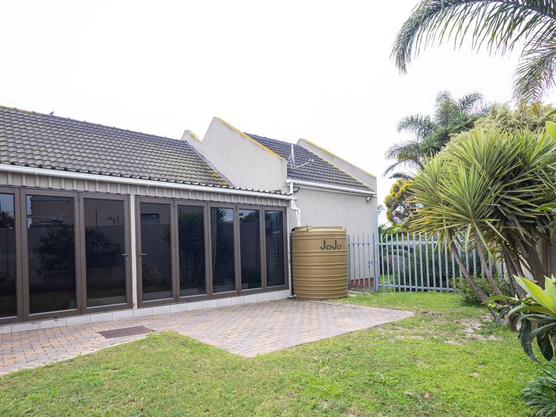 Rear view of the property featuring a paved patio area, large folding glass doors, and a water storage tank set within a private garden.