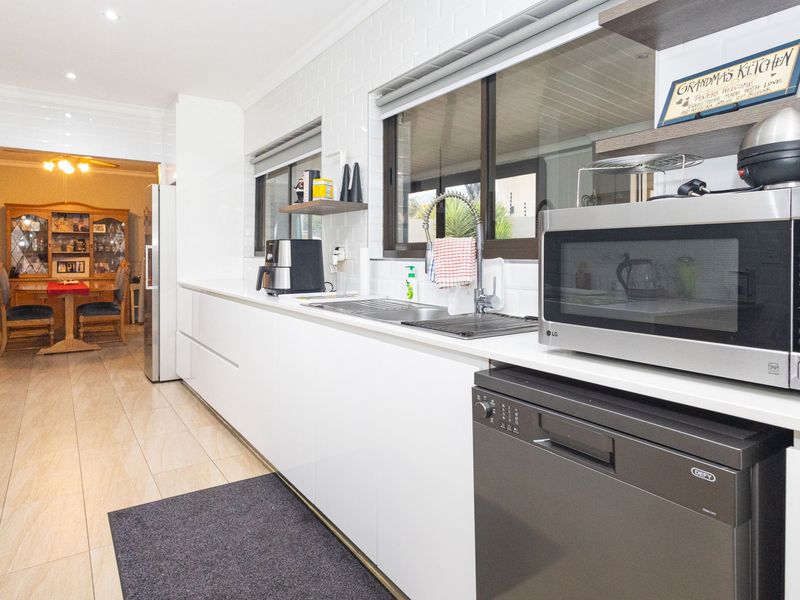 Modern galley-style kitchen featuring sleek white cabinetry, subway tile backsplash, stainless steel sink, and integrated appliances with tiled flooring.