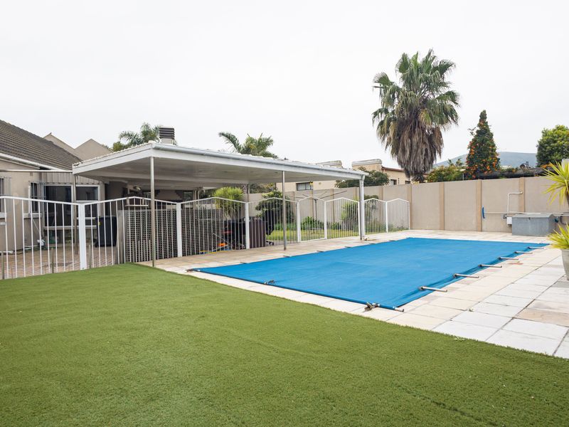 Outdoor pool area featuring a covered patio, paved surround, artificial lawn, and perimeter walling, providing a functional space for outdoor recreation.
