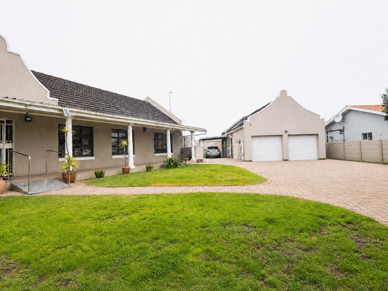 Front view of a single-story house featuring a paved driveway, double garage, covered veranda, and a well-maintained front garden area.