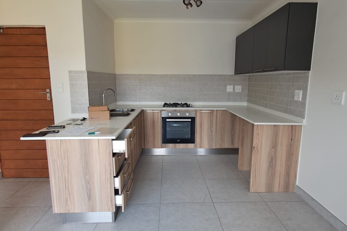 Modern kitchen featuring light wood-grain cabinetry, dark overhead cupboards, stone countertops, built-in oven, gas hob, and neutral tiled flooring in an open-plan layout.