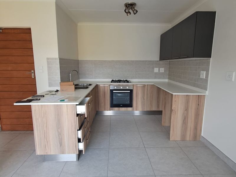 Modern kitchen featuring light wood-grain cabinetry, dark overhead cupboards, stone countertops, built-in oven, gas hob, and neutral tiled flooring in an open-plan layout.