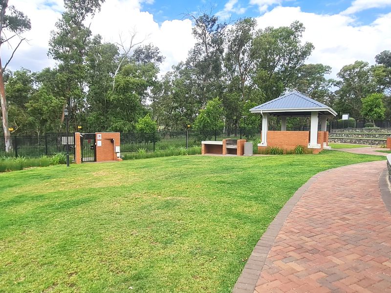 Well-maintained communal garden area featuring a brick gazebo, built-in braai facilities, paved walkways, and stone retaining walls within a secure complex.