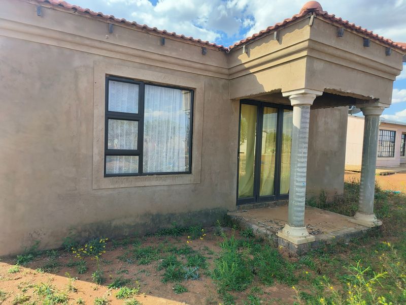 Front elevation of a single-story house featuring a covered porch with concrete columns, aluminium window frames, and a terracotta tiled roof.