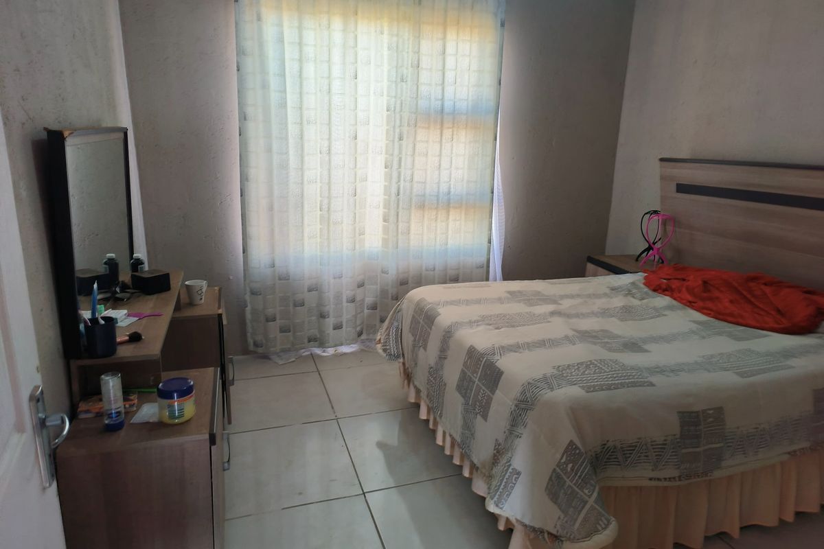 A bedroom featuring tiled flooring and a large window with curtain rails, requiring cosmetic updates to the wall finishes.