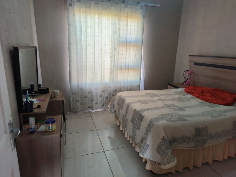 A bedroom featuring tiled flooring and a large window with curtain rails, requiring cosmetic updates to the wall finishes.