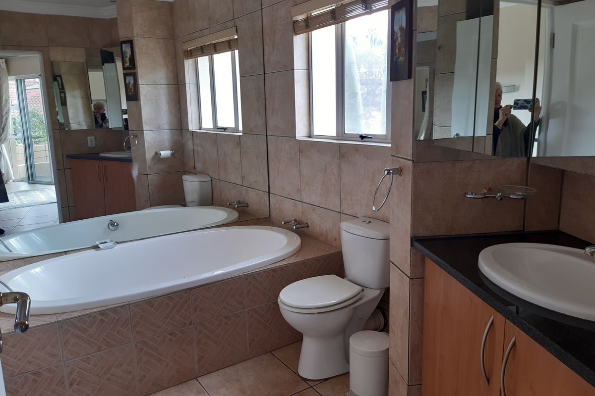 A functional bathroom featuring a built-in vanity, drop-in bathtub, toilet, and extensive wall tiling with large mirrors.