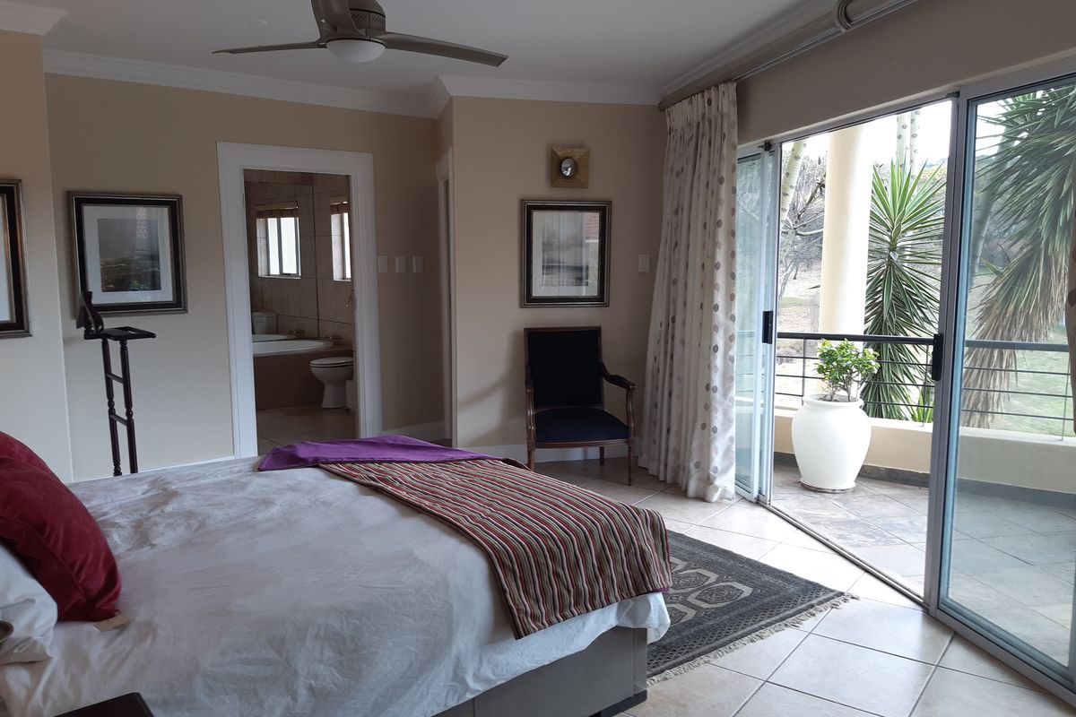 Spacious bedroom featuring tiled floors, a ceiling fan, and large sliding glass doors opening onto a private balcony with en-suite bathroom access.