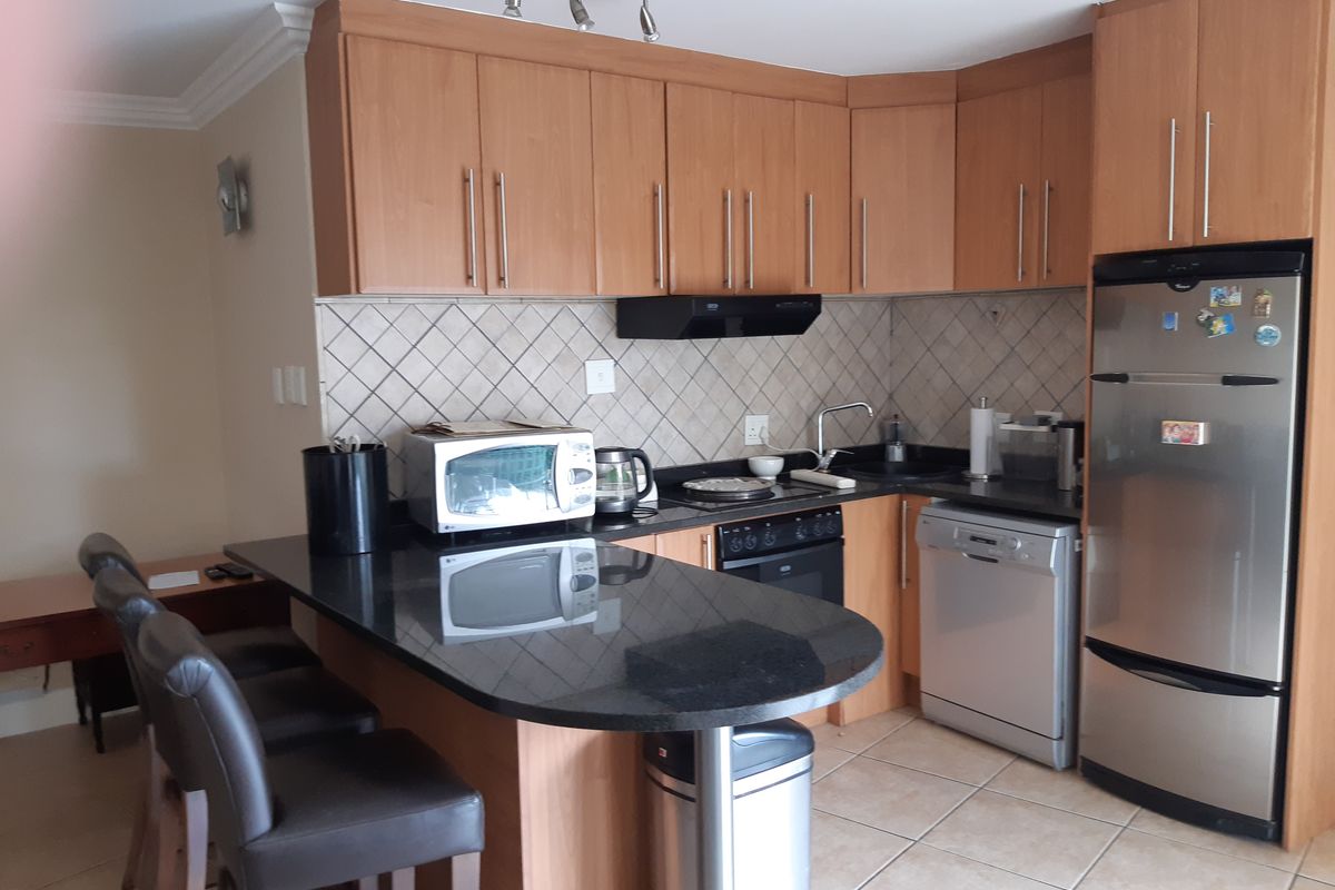 A functional kitchen featuring wood-finish cabinetry, granite countertops, a tiled backsplash, and integrated appliances, including a breakfast bar area.