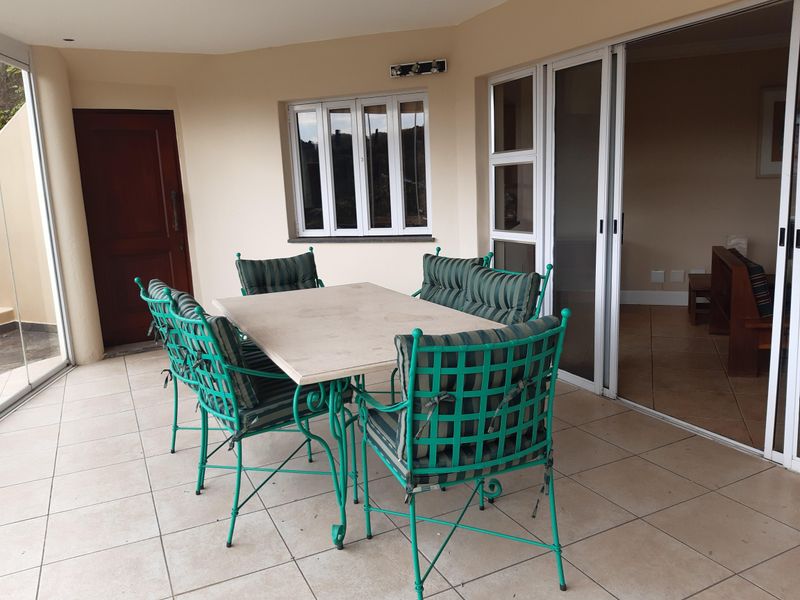 A covered patio area featuring tiled flooring, sliding glass doors leading to the interior, and a casement window, providing a functional outdoor entertainment space.