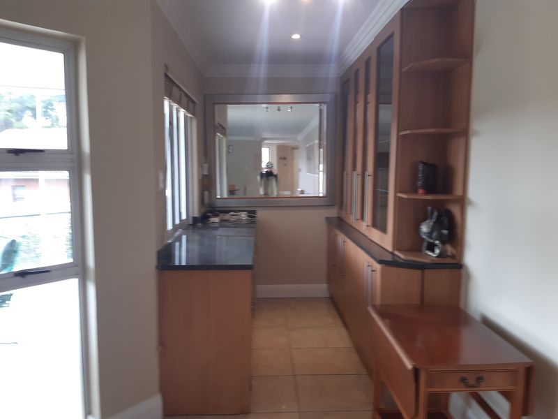 A functional scullery area featuring built-in wooden cabinetry, granite countertops, tiled flooring, and large windows providing natural light.