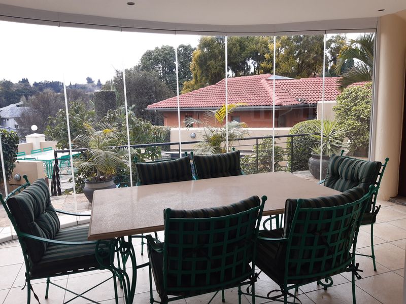 A covered patio featuring a frameless glass enclosure, tiled flooring, and recessed lighting, offering a pleasant view of the surrounding garden and neighborhood.