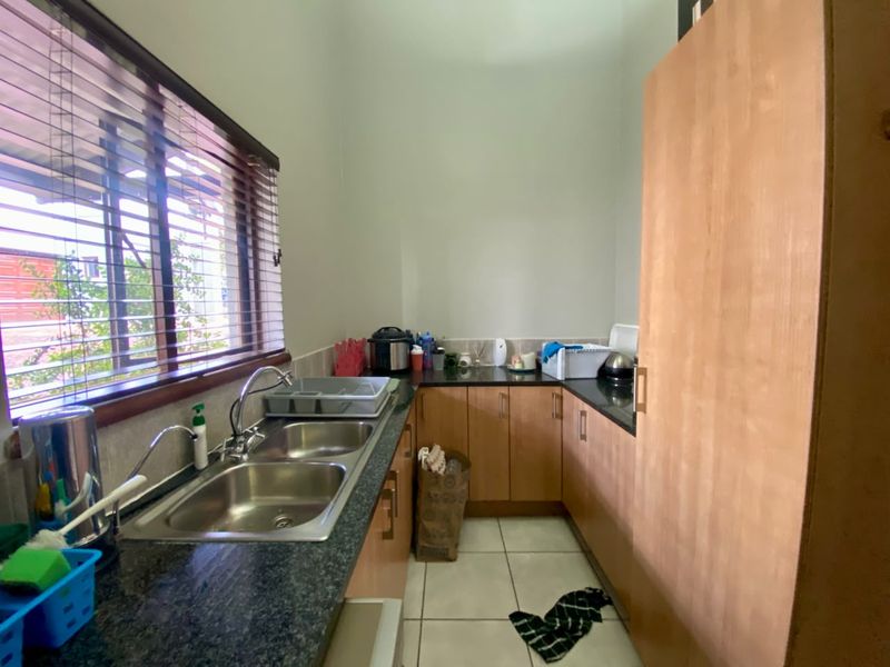 A functional scullery featuring laminate cabinetry, granite countertops, a double stainless steel sink, and tiled flooring, providing additional prep and wash-up space.