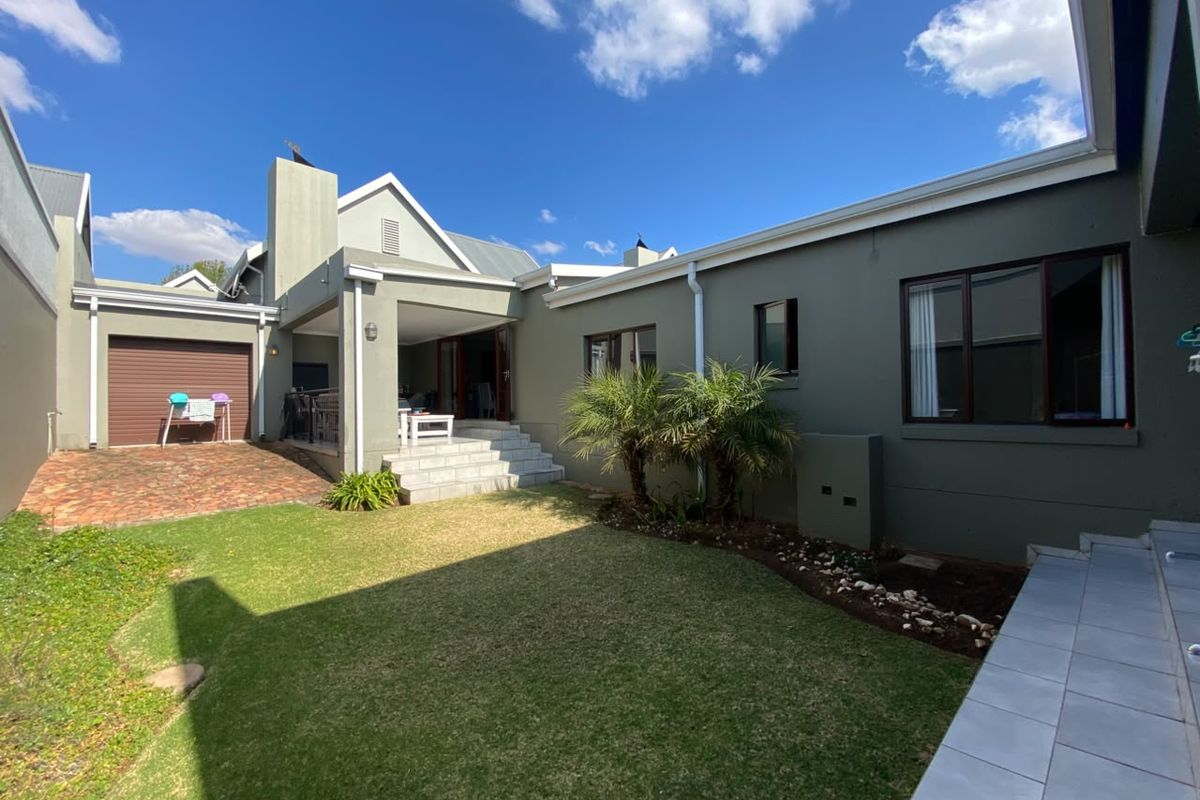 A well-maintained rear exterior view featuring a lawn, covered patio area, paved driveway, and access to the garage.