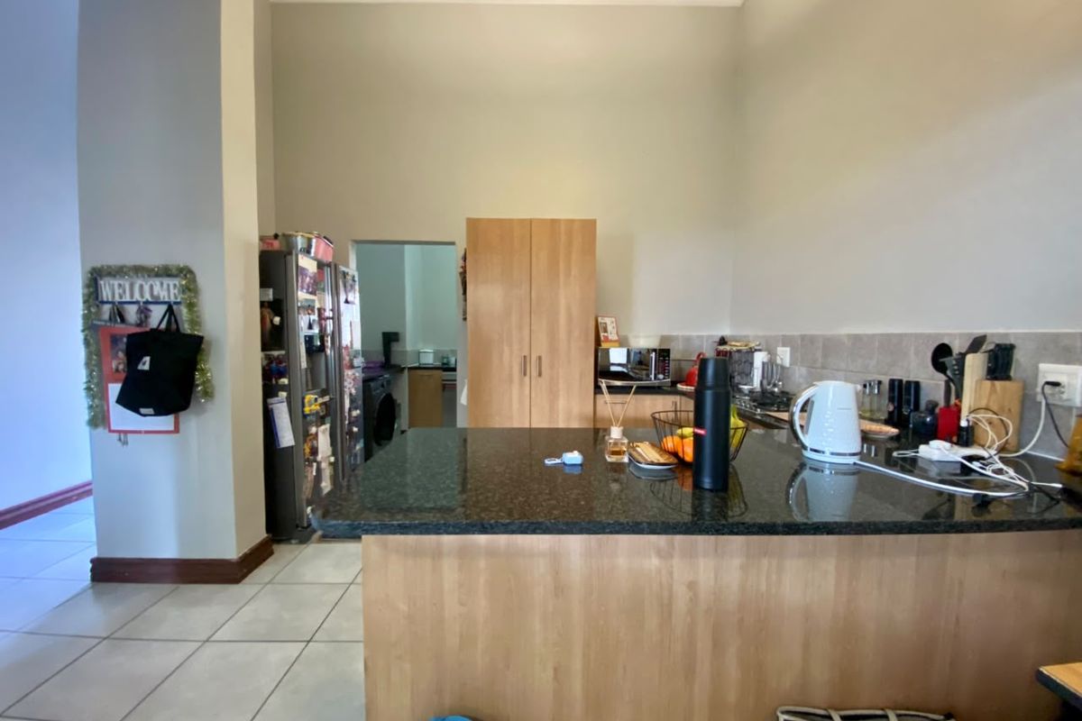 A functional kitchen featuring granite countertops, wood-finish cabinetry, and a tiled backsplash, with an adjacent scullery area visible in the background.