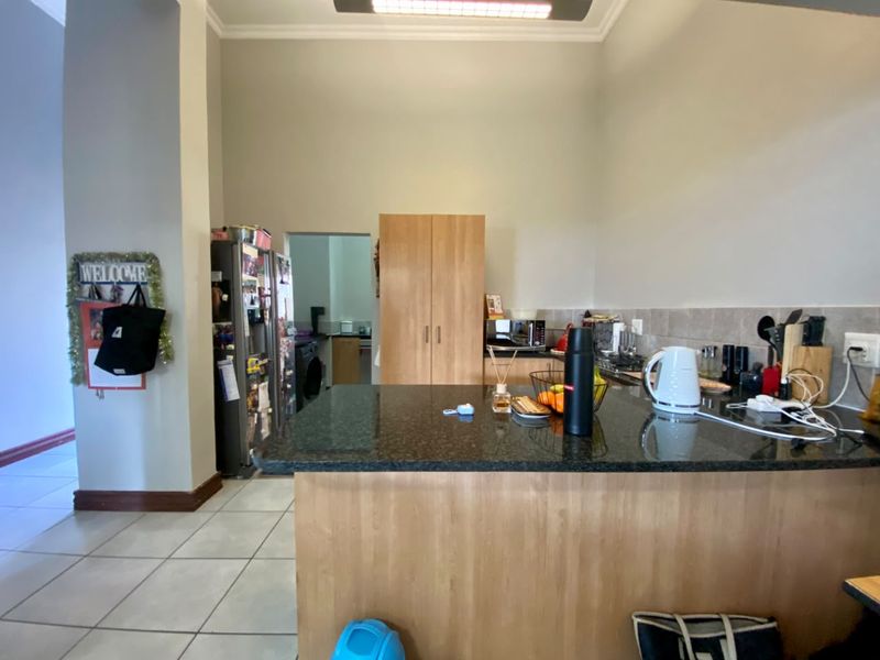 A functional kitchen featuring granite countertops, wood-finish cabinetry, and a tiled backsplash, with an adjacent scullery area visible in the background.
