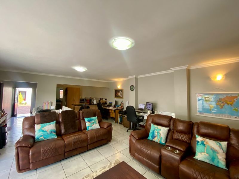 Spacious open-plan living area featuring tiled flooring, cove cornicing, and integrated lighting, seamlessly connecting to a functional kitchen space.