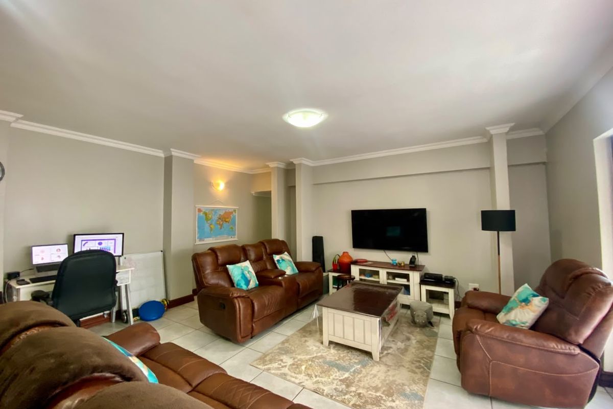 A spacious living room featuring tiled flooring, crown molding, and a wall-mounted television, providing a functional and comfortable family entertainment area.