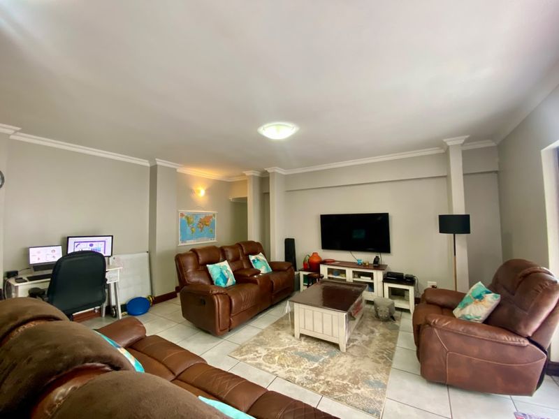 A spacious living room featuring tiled flooring, crown molding, and a wall-mounted television, providing a functional and comfortable family entertainment area.