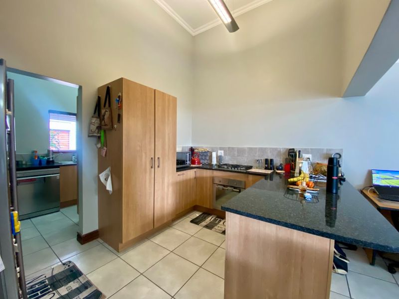 Open-plan kitchen featuring light wood cabinetry, granite countertops, built-in oven, and gas hob, with an adjacent scullery area and tiled flooring throughout.