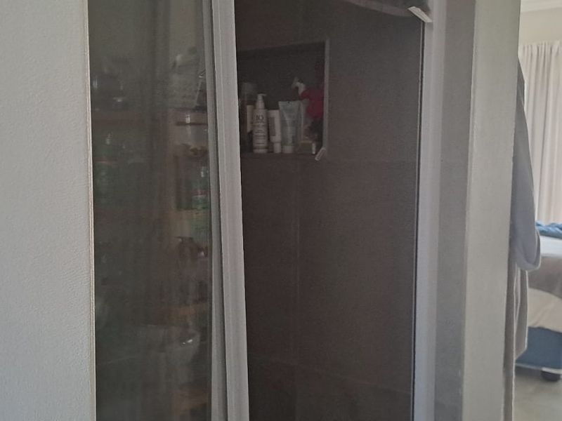 A bathroom featuring a shower enclosure with a built-in tiled niche, adjacent to a bedroom area with sliding door access.