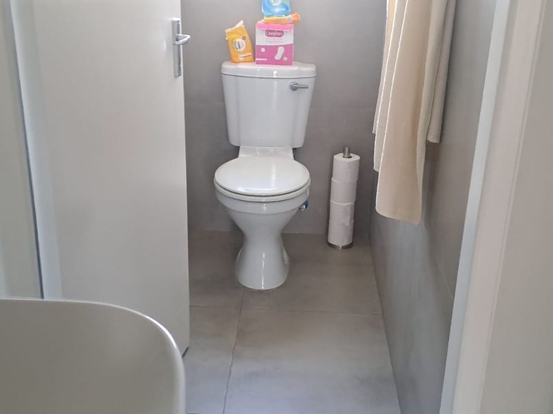 A compact bathroom featuring neutral wall and floor tiles with a standard white toilet suite.
