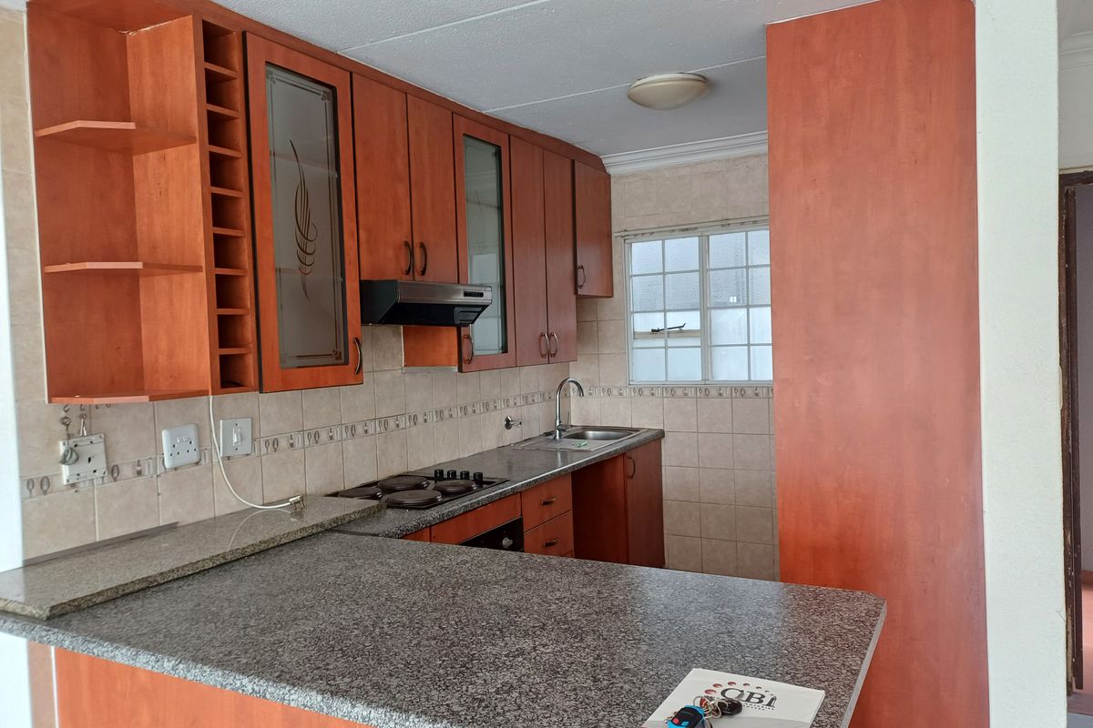A functional kitchen featuring wood-finish cabinetry, granite countertops, a built-in hob and oven, and a convenient breakfast bar for casual dining.