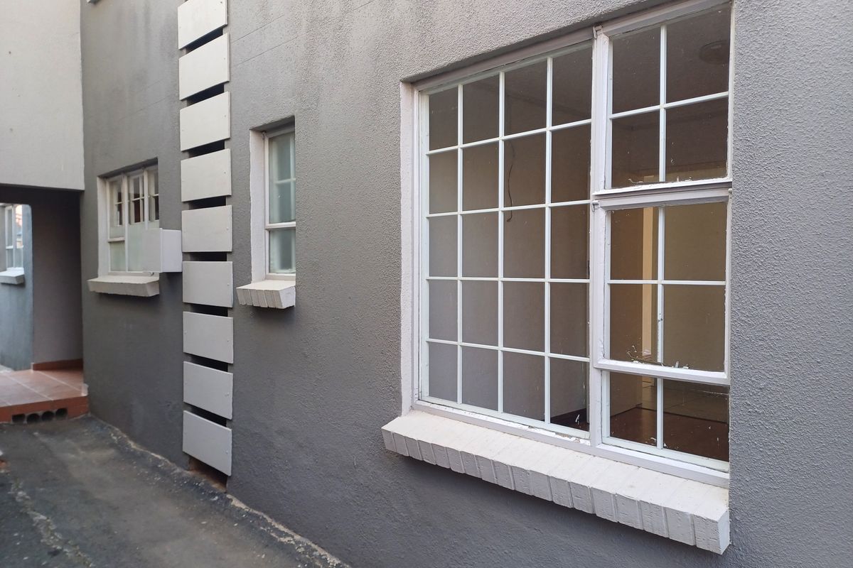 Exterior view of the apartment building showing grey masonry walls, white metal-framed windows with security bars, and visible signs of exterior wear.