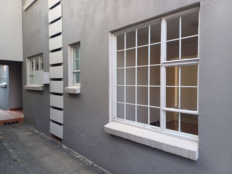 Exterior view of the apartment building showing grey masonry walls, white metal-framed windows with security bars, and visible signs of exterior wear.