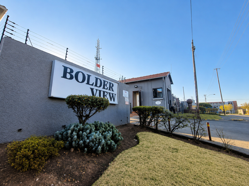 The entrance to Bolder View apartment complex featuring a secure perimeter wall with electric fencing and a dedicated guard house.