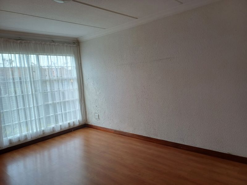 An empty bedroom featuring laminate flooring, textured walls, and a large window with sheer curtains, providing a blank canvas for potential interior design updates.