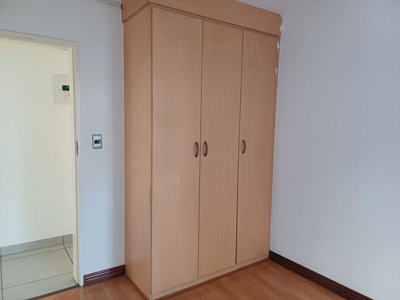 A bedroom featuring light wood-finish built-in wardrobes, laminate flooring, and neutral walls, offering a clean and functional space ready for personalization.
