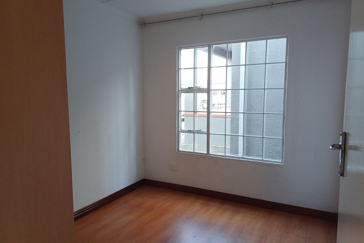 A clean, empty bedroom featuring laminate flooring, white walls, and a window fitted with security burglar bars.