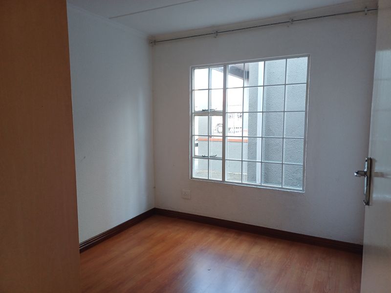 A clean, empty bedroom featuring laminate flooring, white walls, and a window fitted with security burglar bars.