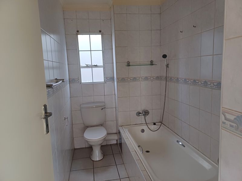 A functional bathroom featuring a bathtub with shower mixer, toilet, and tiled finishes throughout, offering a blank canvas for potential modernization.